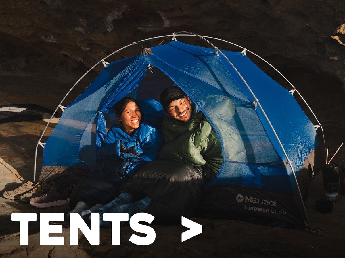 Two campers relaxing inside a blue tent outdoors, labeled “Tents.”