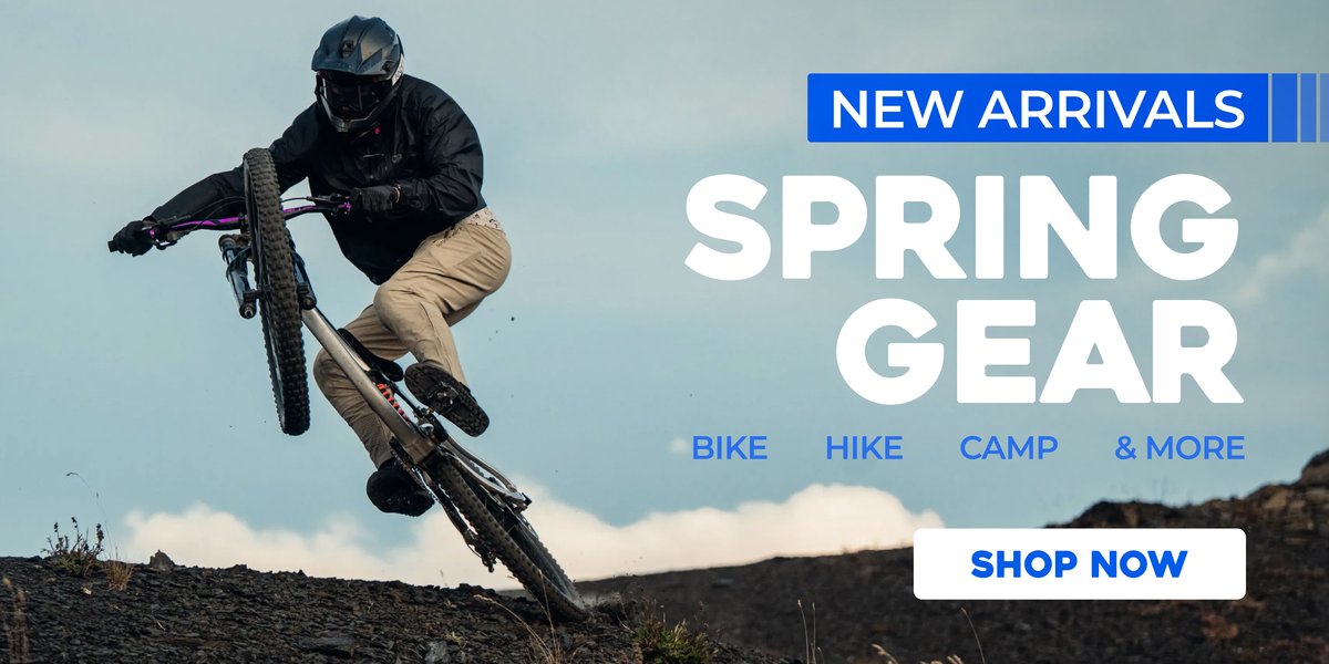 Mountain biker mid-jump on a rocky trail with text promoting new spring gear and a “Shop Now” button.